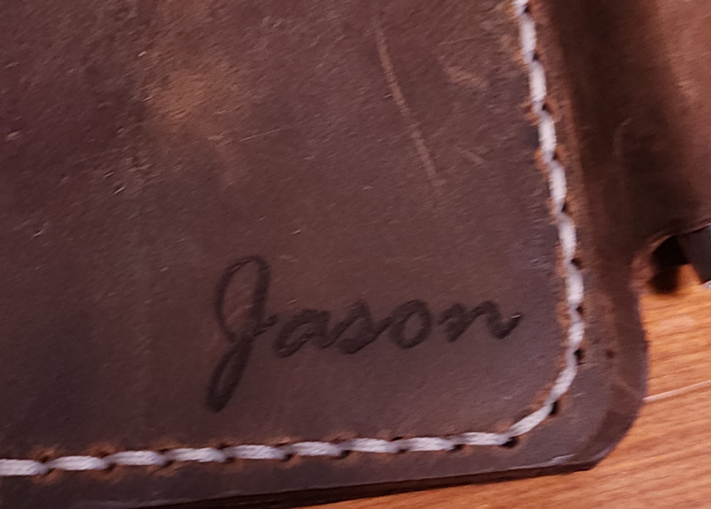 Close-up of full grain leather field notes cover personalized with the name Jason and white stitching